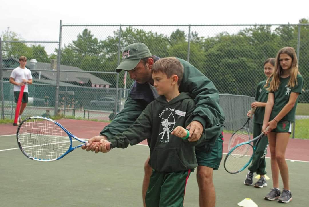 Coach guiding a young camper's forehand